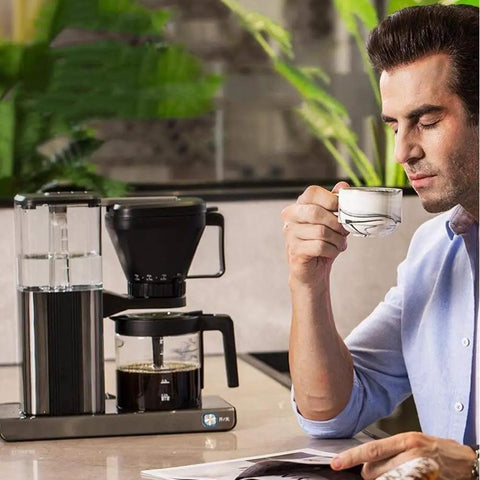 Heavy Duty Fully Automatic Espresso And Drip Coffee Maker With Digital Display Six Steam Nozzles For Killer Brews 10 Cup Glass Carafe in use with a man drinking coffee.