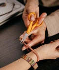 Premier No 5 Micro Tip Orange Handled Fabric Scissors With Double Loop Handle being used for detailed cutting on bracelet string.