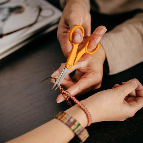 Premier No 5 Micro Tip Orange Handled Fabric Scissors With Double Loop Handle being used for detailed cutting on bracelet string.