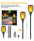 4 Pack 43 Inch Solar Torch Lights With 96 LEDs, Outdoor Waterproof Landscape Pathway Lighting, Realistic Flickering Flame Effect For Patio Vibes, Dusk To Dawn Auto On Off, Yard Garden Decor installed along a garden path.