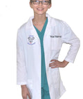 Kids Veterinarian Lab Coat With Embroidered Name And Puppy Embroidery White Size 12/14 Unisex 3 Pockets 65 Percent Polyester And 35 Percent Cotton Machine Washable Realistic Vet Role Play Outfit For Aspiring Pet Doctors worn by a child