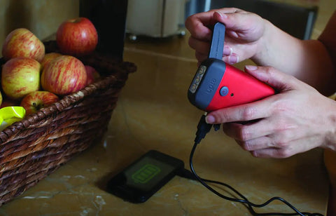 Person using Clipray Clip On Hand Crank Flashlight And Phone Charger For Emergency Prep No Batteries Needed One Minute Crank Delivers Ten Minutes Of Bright LED Light Cherry Red, charging phone.