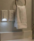Illuminated Night Light Wall Switch Pack beside outlet and towel, single pole, 15A 120/277V, white, bathroom installation