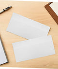 100 Pack White Self Seal Envelopes With Release Paper For Privacy Protection on a wooden office desk