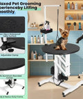 Elevate Your Grooming Game With This Heavy Duty Electric Hydraulic Pet Table Featuring A Rotating Waterproof Top, Remote And Foot Pedal Height Adjustments For Easy Back Saving Lifts Up To 250 Lbs Plus An Overhead Arm Tool Organizer System. A small dog sits on a black waterproof pet grooming table with adjustable clamp in a salon setting.