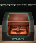 Creality laser engraver enclosure front view; black cabinet with green-lit window and integrated fan