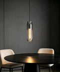 PRTSER 11.8" Modern Pendant Light Fixture with Smoke Gray Crystal Lampshade hangs above a round black table and beige chairs.