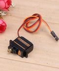 Four Pack ES08MA II 12g Mini Metal Gear Analog Servo for RC Models on wooden surface with flowers, compact size displayed