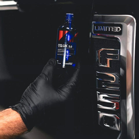 Carpro CQUARTZ UK 3.0 ceramic coating bottle, 50ml kit, held by gloved hand beside a car door handle
