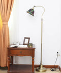 Vintage Tiffany Style Floor Lamp With Grape Stained Glass Shade Arched Gooseneck Reading Light On Bronze Pole Corner Standing Design For Bedroom And Living Room Decor Vibe next to a wooden table by curtains.