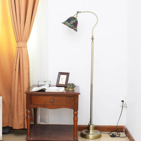 Vintage Tiffany Style Floor Lamp With Grape Stained Glass Shade Arched Gooseneck Reading Light On Bronze Pole Corner Standing Design For Bedroom And Living Room Decor Vibe next to a wooden table by curtains.
