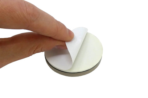 Close-up of a hand peeling adhesive backing from a circular glide, part of Four Pack Nail On 1 Inch Swivel Furniture Glides.