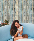 Woman seated in front of Blue Distressed Wood Grain Self Adhesive Contact Paper Peel And Stick Waterproof Wood Wallpaper For Cabinets And Walls Removable Reno Ready Home Makeover Easy Install Fifteen Point Seven By Three Hundred Ninety Four Inches.