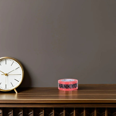 Pink Packing Tape Roll Set For Shipping Boxes, 7 Rolls, 100 Yard Each, Heavy Duty Moisture Resistant Sealing Tape For Moving And Packaging, Built Tough, Easy Tear, Ideal For Boxes Bags And Mailers on table beside clock