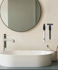 Bathroom sink area with round mirror and adhesive toothbrush and razor holders mounted on wall