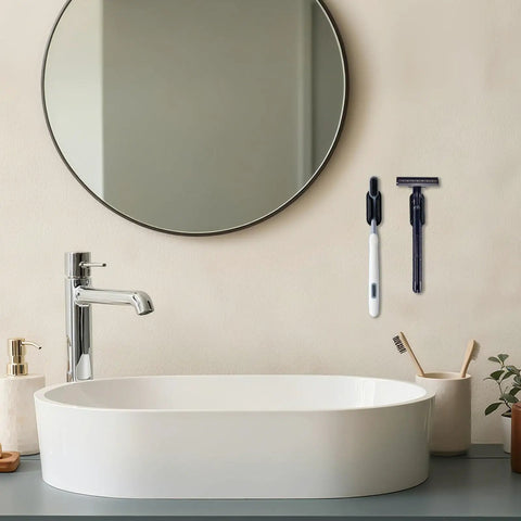Bathroom sink area with round mirror and adhesive toothbrush and razor holders mounted on wall