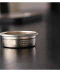 Premium Titanium Portafilter Basket 58.5mm holds 18 to 20 grams on a wooden surface for home baristas.