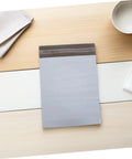 White Poly Mailers 10x14 Inch Waterproof Self Seal Shipping Bags For Apparel And Clothes lying on a wooden surface