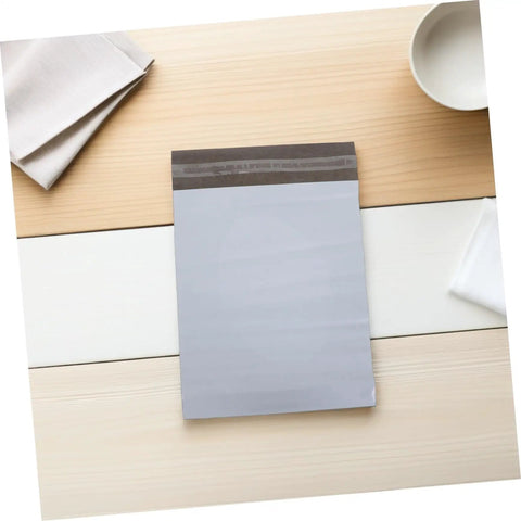 White Poly Mailers 10x14 Inch Waterproof Self Seal Shipping Bags For Apparel And Clothes lying on a wooden surface