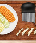 Crinkle cutter knife with stainless blade and black handle on a wooden board; plate of orange, yellow, and green crinkle-cut slices.