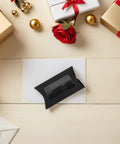 A single box from 50 Pack Black Kraft Paper Pillow Gift Boxes With Window For Birthday Parties And Events on a table surrounded by gifts.