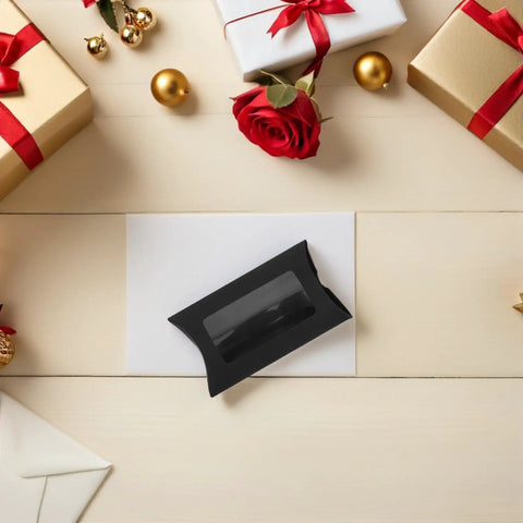 A single box from 50 Pack Black Kraft Paper Pillow Gift Boxes With Window For Birthday Parties And Events on a table surrounded by gifts.