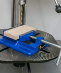 4 Inch Drill Press Vise For Your Home Shop Portable Bench Vise with slotted base in cast iron, holding a wooden block on drill table.