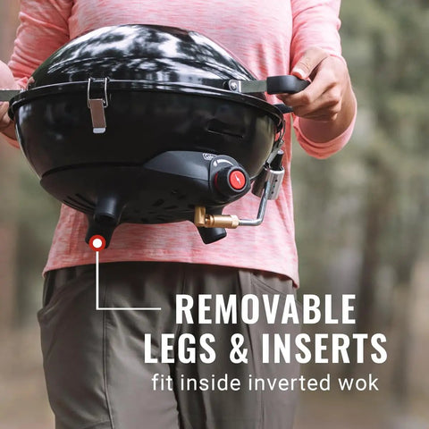 Person holding Four In One Portable Propane Grill With Stove Griddle And Wok Attachments, showing removable legs in inverted wok