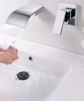 Waterfall Wall Mount Tub Faucet In Brass With Chrome Finish above a white basin, water flowing smoothly, hands catching water
