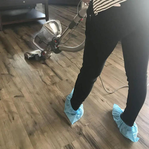 Person wearing Disposable Shoe Covers X Large 100 Pack Of 50 Pairs Non Slip Floor Protection while cleaning with vacuum cleaner.