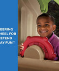 Child playing with red steering wheel on Tot Friendly Outdoor Kids Playset With Two Tier Swing Set, Slide, Climber, Crawl Space And Playhouse.