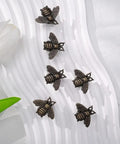 Set of six vintage bee cabinet pulls on a textured surface, antique polished beehive drawer handles for home decor.