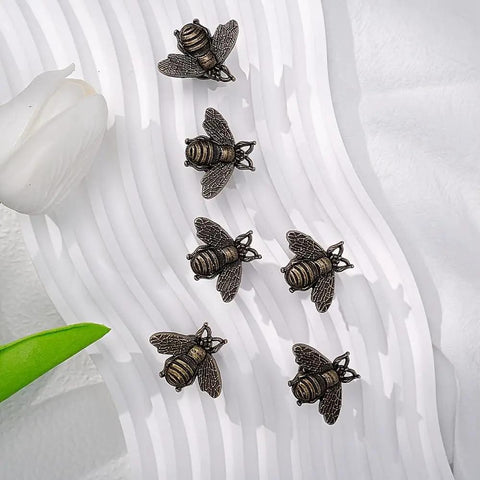 Set of six vintage bee cabinet pulls on a textured surface, antique polished beehive drawer handles for home decor.