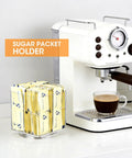 No Sweat Spin Lazy Susan Drink Packet Organizer Square Four Compartment Pantry Turntable For Water Flavor Drinks Sugar Packets Honey Sticks And Tea Bags Kitchen Countertop with sugar packets next to coffee machine.