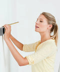 Woman using OSPSHPG Multifunctional Wall Scanner to detect studs and wires on a wall with a pencil in hand.