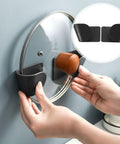 Hands placing lid on Wall Mounted Pot Lid Organizer Rack For Lids And Cutting Boards ABS Black Universal Lid Holder No Drill Perforation Free Design Heavy Duty Kitchen Storage Strong Load Bearing Capacity