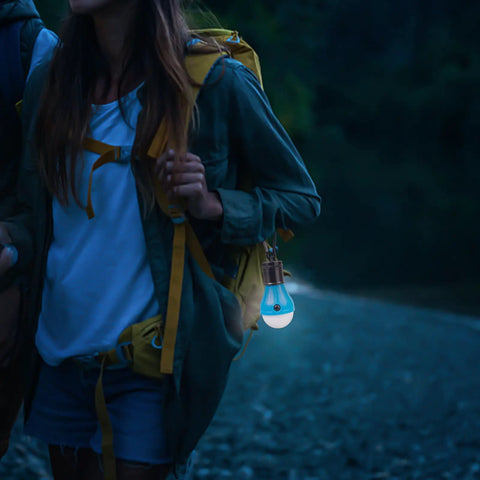Person hiking at night with Go-To USB Rechargeable LED Camping Lanterns Four Pack With Clip Hook Hanging Design For Outdoor Tent Lighting.