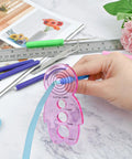 Person using 12 Piece Slotted Quilling Tool Set for Paper Crafting with pink template and blue strip on marble table.