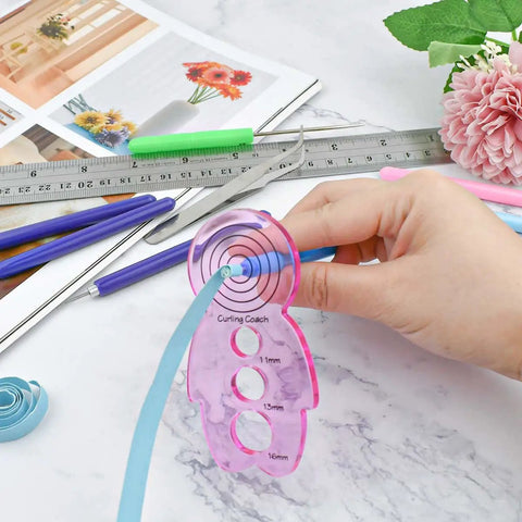 Person using 12 Piece Slotted Quilling Tool Set for Paper Crafting with pink template and blue strip on marble table.