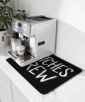 Spooktacular Black Witches Brew Coffee Station Mat Featuring Quick Dry Absorbent PU Material Designed For Kitchen Counter Espresso Machine Setup 28 By 18 Inch Halloween Spill Proof Drip Catch Pad on countertop.