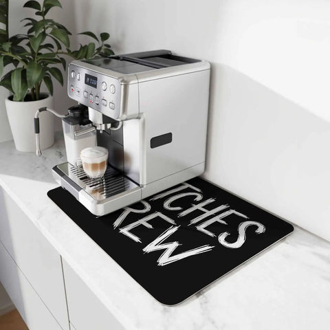 Spooktacular Black Witches Brew Coffee Station Mat Featuring Quick Dry Absorbent PU Material Designed For Kitchen Counter Espresso Machine Setup 28 By 18 Inch Halloween Spill Proof Drip Catch Pad on countertop.