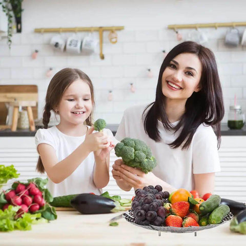 Mother and daughter in kitchen with Premium Stainless Steel Veggie Steamer Basket filled with fruits and vegetables.