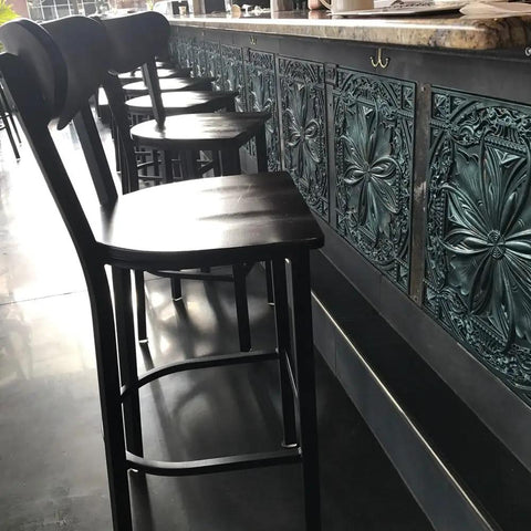 Bar area with black chairs and decorative paneling, showcasing the Dope 2x2 PVC Ceiling Tile Set Patina Finish