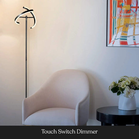 Halo Split LED Torchiere floor lamp in jet black with dimmable rotating light rings beside modern living room chair and table.