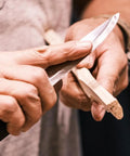 Person using Companion Carbon Steel Fixed Blade Knife With Sheath 4.1 Inch Blade Military Green for whittling wood outdoors.
