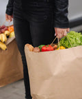 Person carrying groceries in DIY Grocery Paper Bags 200 Pack 14x10x15.75 Inch Kraft Color With Handles 110 GSM Thick And Strong Recyclable