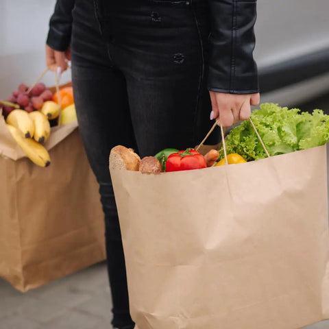 Person carrying groceries in DIY Grocery Paper Bags 200 Pack 14x10x15.75 Inch Kraft Color With Handles 110 GSM Thick And Strong Recyclable