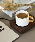 Electric Coffee Mug Warmer With Three Heat Settings And Four Hour Auto Shutoff Keeps Your Favorite Brew Piping Hot For Lazy Desk Setup Or Cozy Kitchen Counters No More Cold Sip Vibes On The Daily with a white mug on a wooden warming tray next to a laptop.