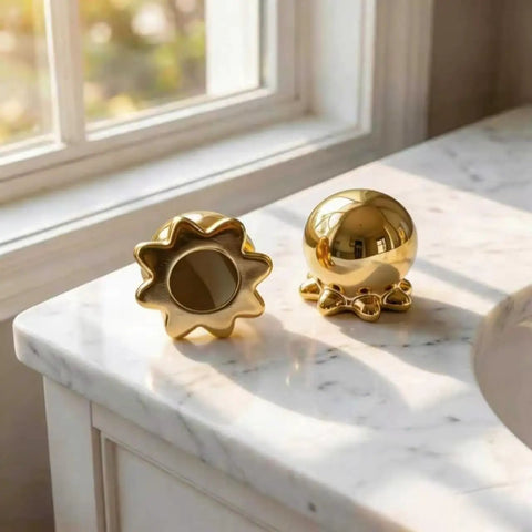 Darn Slick Ceramic Gold Octopus Toilet Bolt Caps Two Pack Snazzy Bathroom Screw Covers on marble counter with sunlight.
