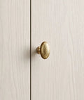 Close-up of Top Shelf Champagne Bronze Cabinet Knob with Hammered Oval Dome on light wood cabinet door surface.
